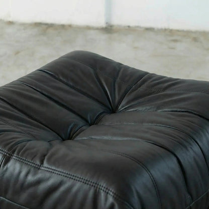 Close-up of a black Bruma leather ottoman with a blurred background