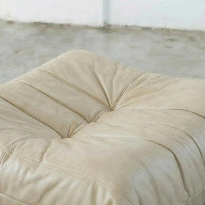 Beige Bruma leather ottoman on a concrete floor with white walls