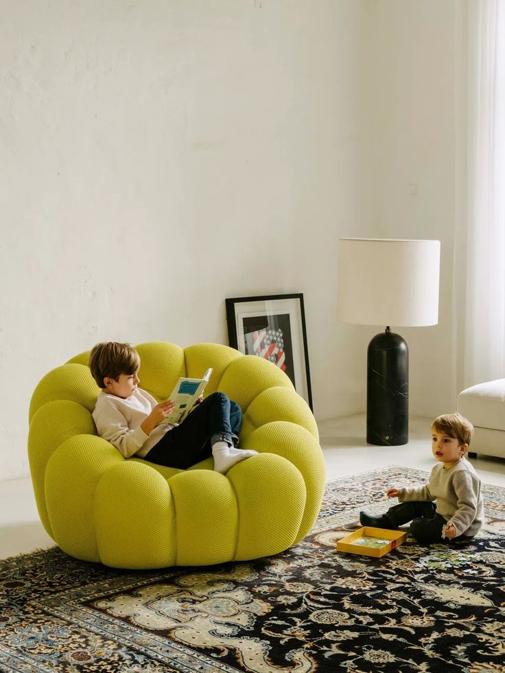 Two children in a living room with a yellow bubble armchair replica and a lamp.