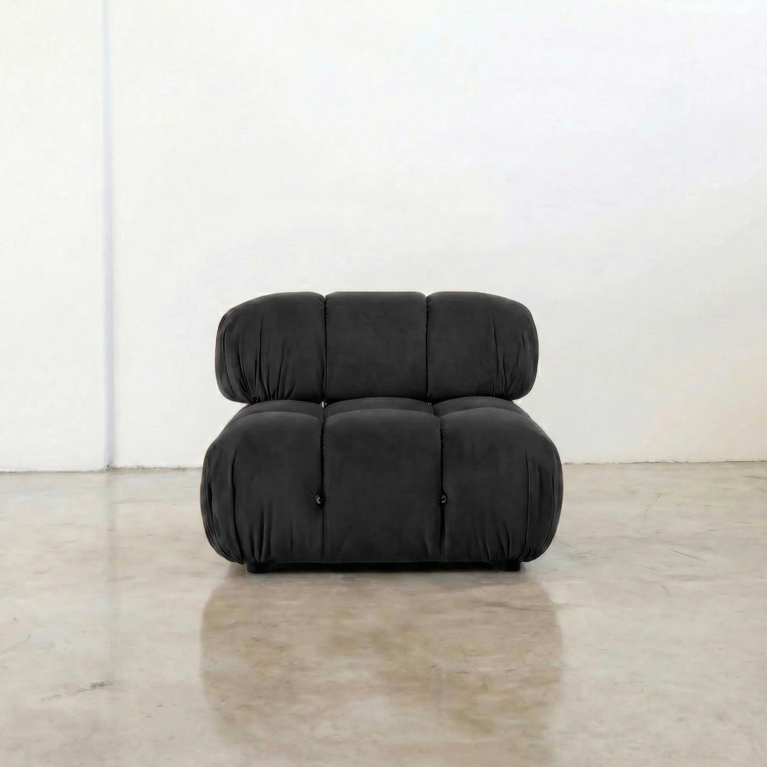 Dark gray camaleonda velvet armless section in a minimalistic room with a white wall and concrete floor.