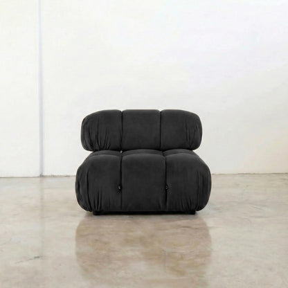 Dark gray camaleonda velvet armless section in a minimalistic room with a white wall and concrete floor.