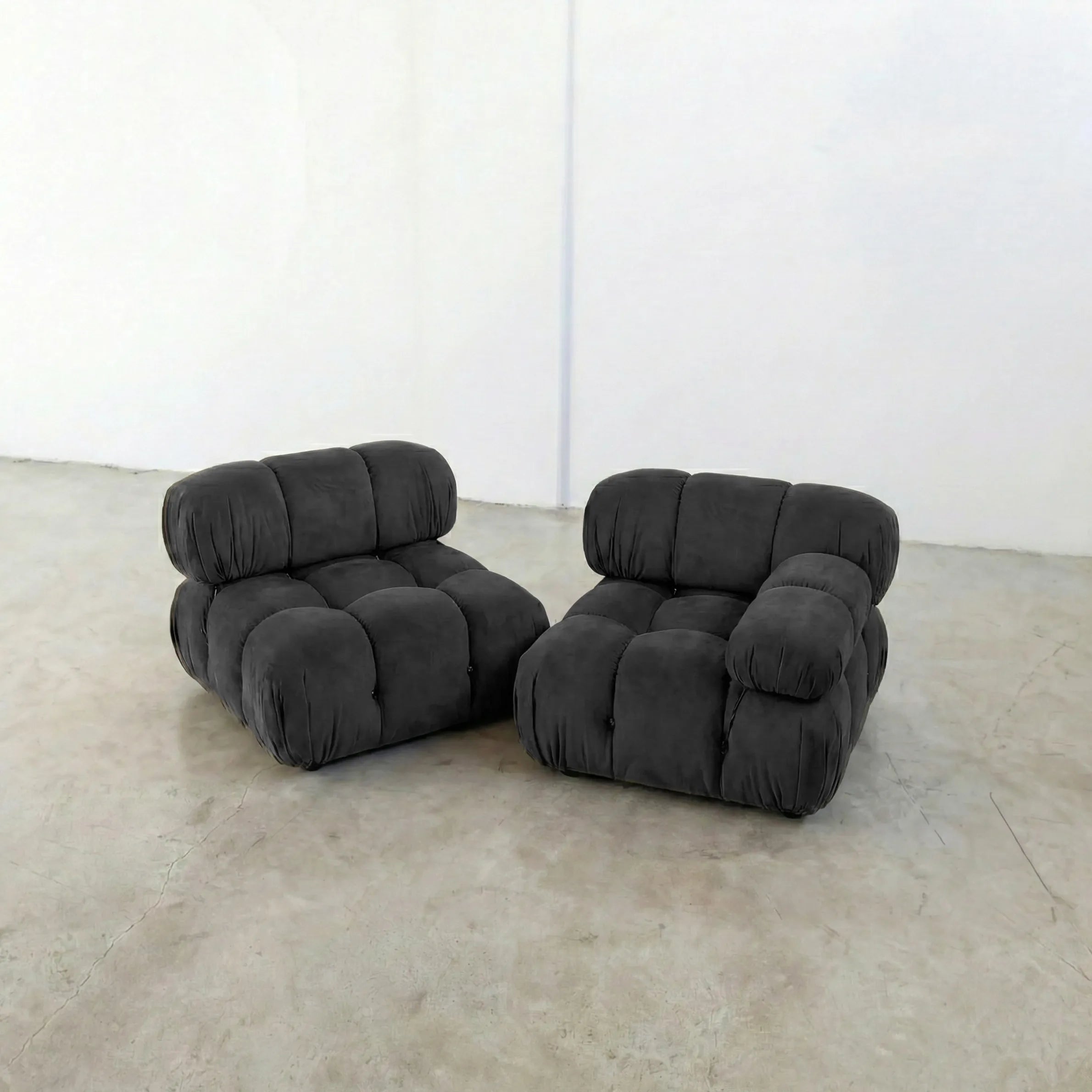 Two dark gray camaleonda dupe inspired armchairs on a beige floor with a white wall background