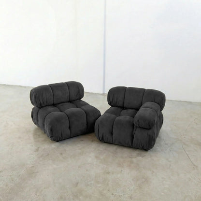 Two dark gray camaleonda dupe inspired armchairs on a beige floor with a white wall background