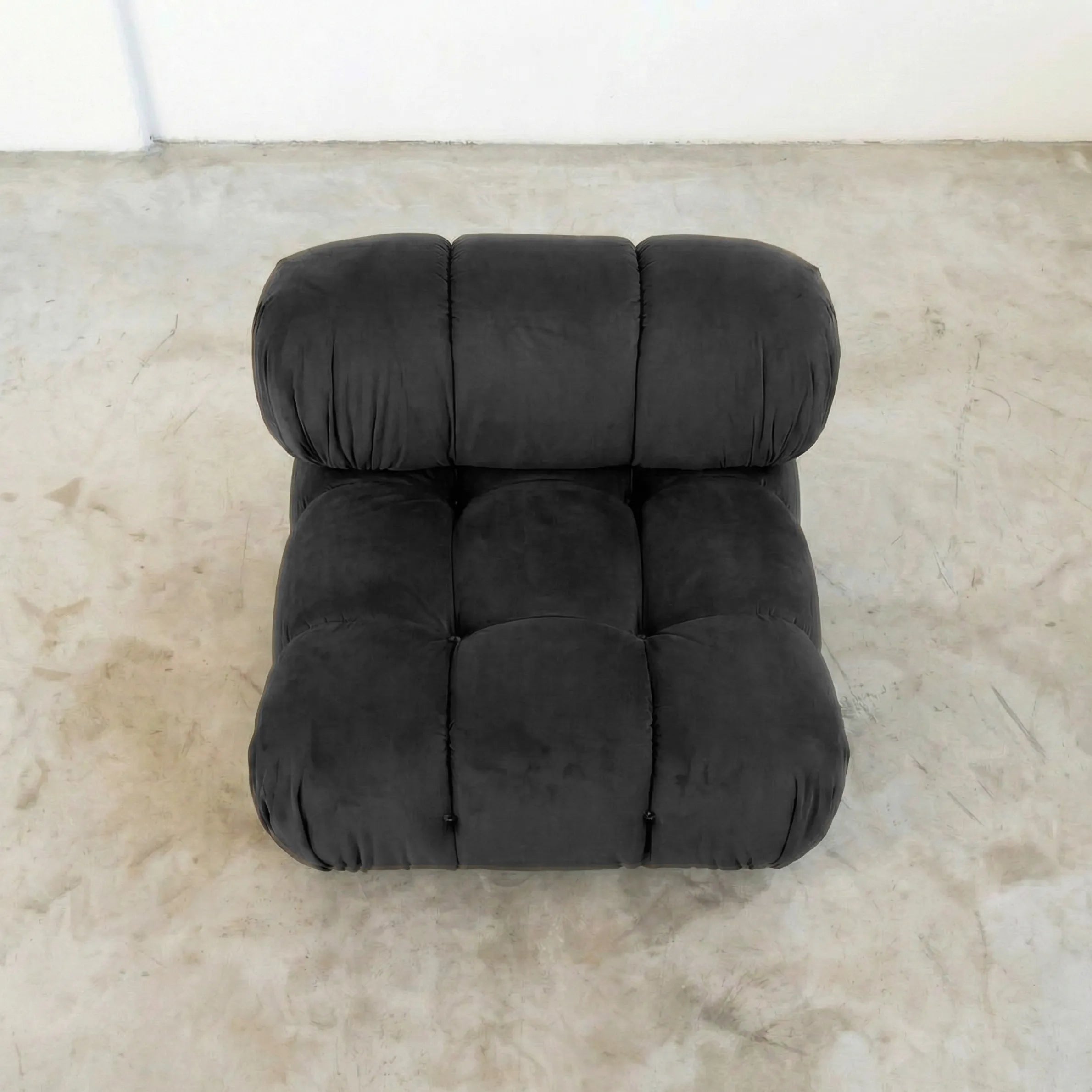 Dark gray camaleonda dupe velvet armless section in a minimalistic room with a white wall and concrete floor.