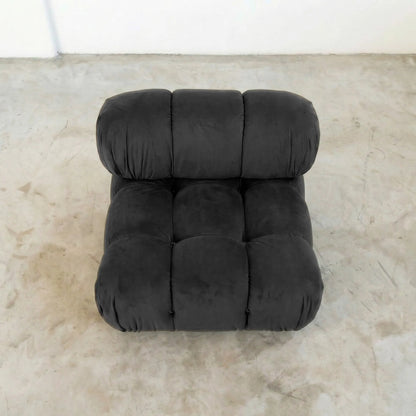 Dark gray camaleonda dupe velvet armless section in a minimalistic room with a white wall and concrete floor.