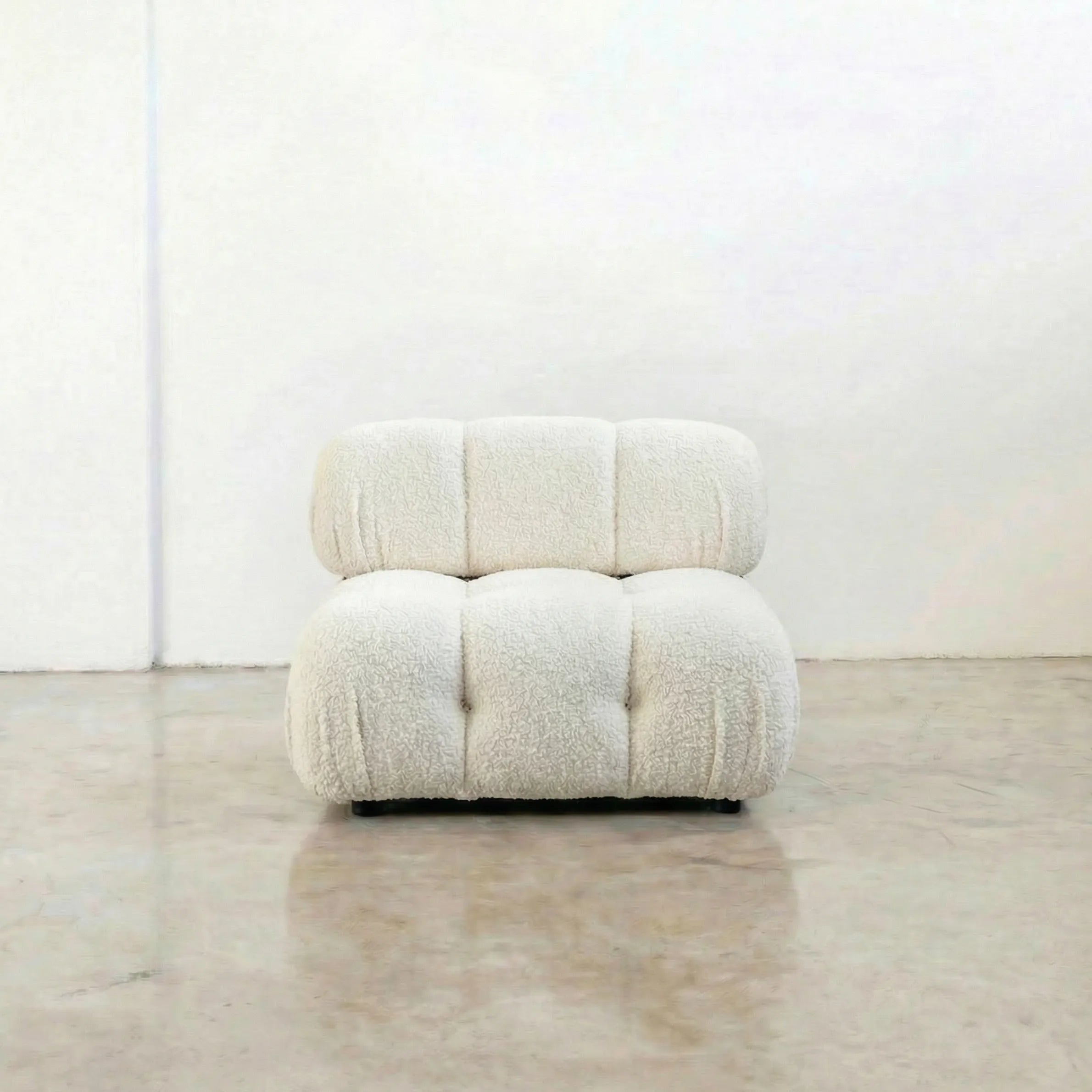camaleonda dupe armchair in white boucle on a reflective floor with a white wall background