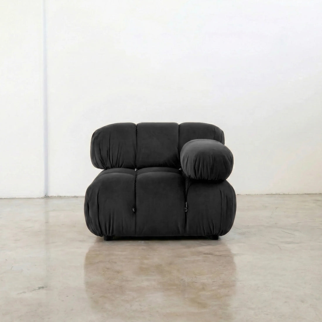 Camaleonda dupe section with armrest in dark grey velvet  in a minimalistic room with white walls and wooden floor.