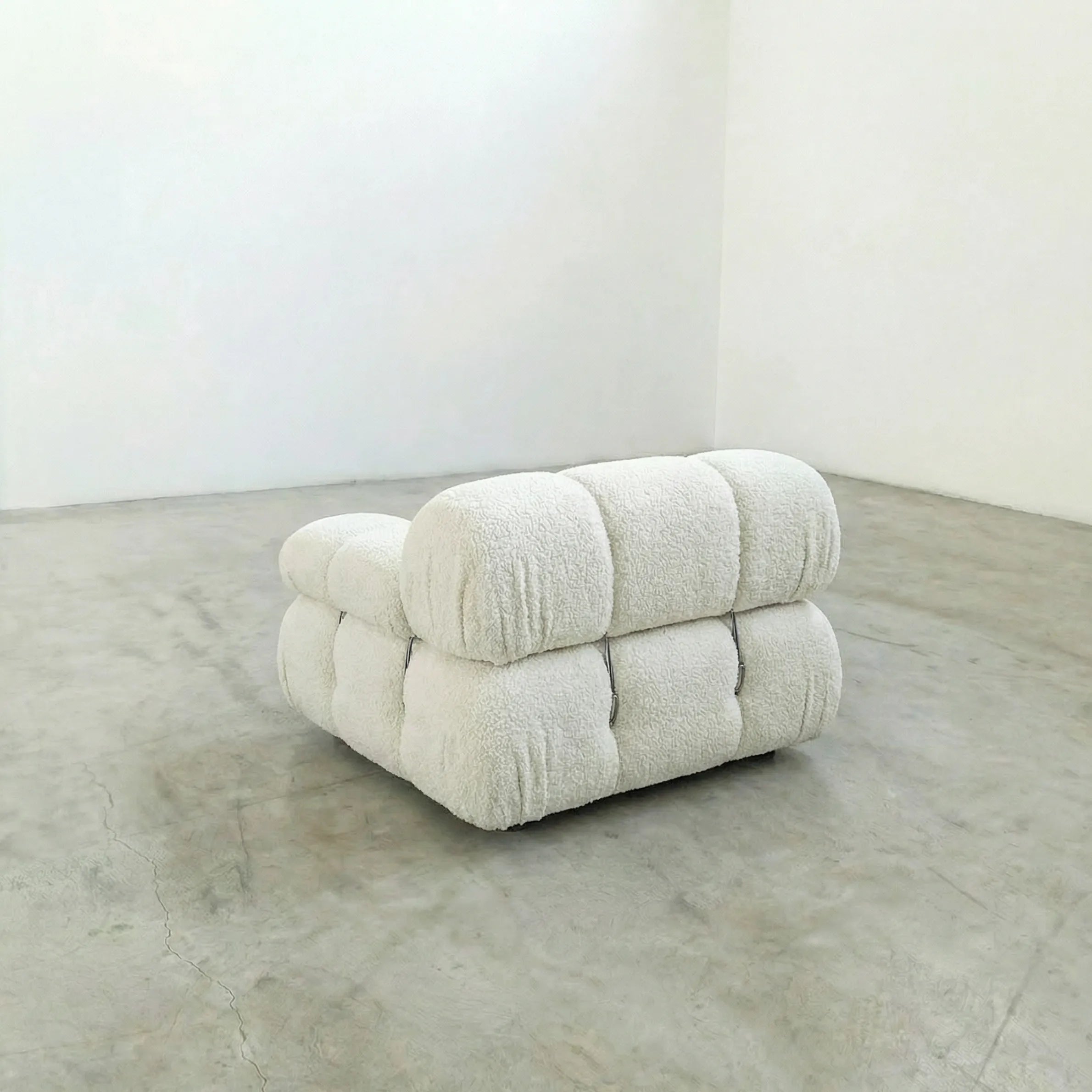 camaleonda armchair dupe with left artmrest in white bouclé  on a concrete floor with white walls
