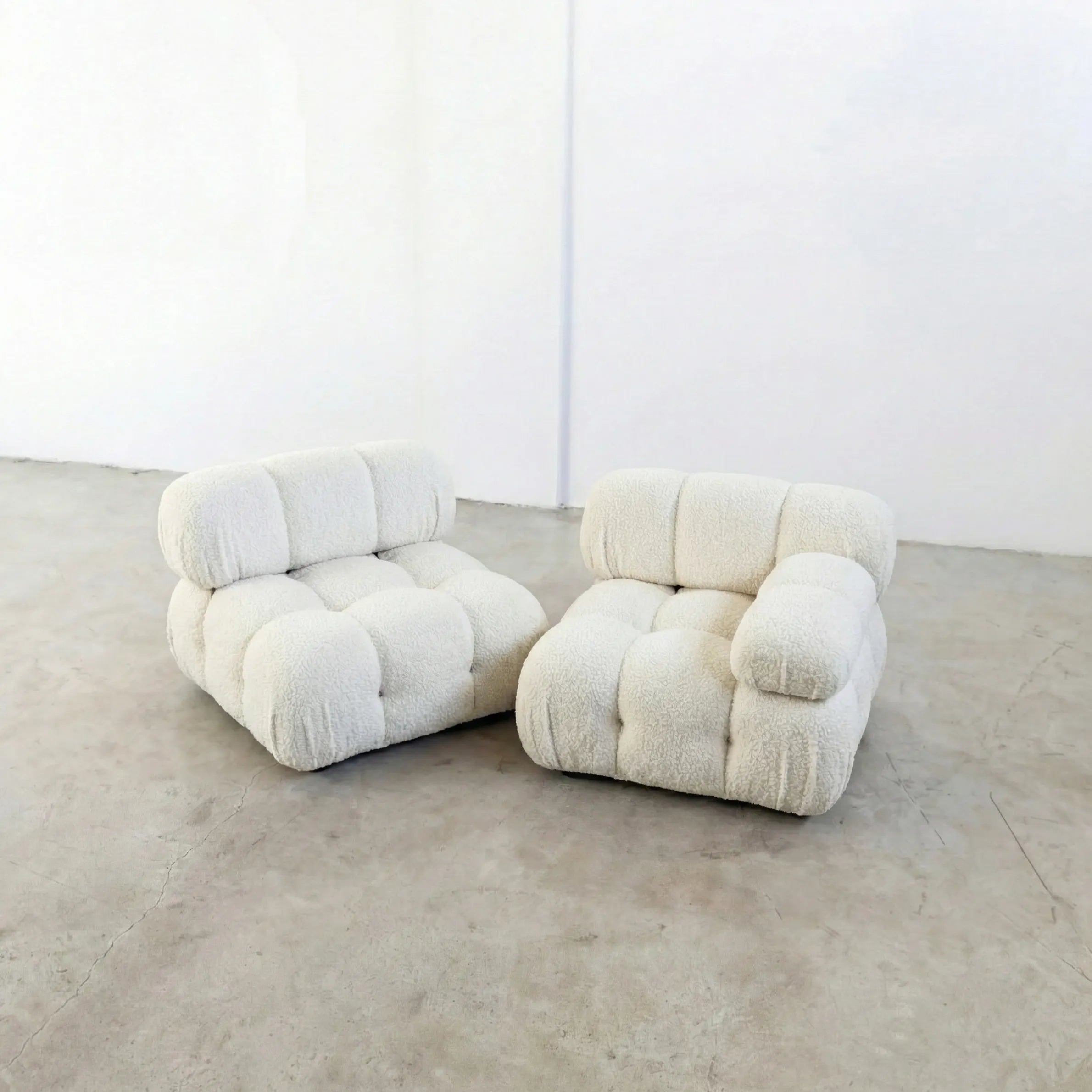 Pair of white modular camaleonda sofa section armchairsin white bouclé on a concrete floor with a white wall background