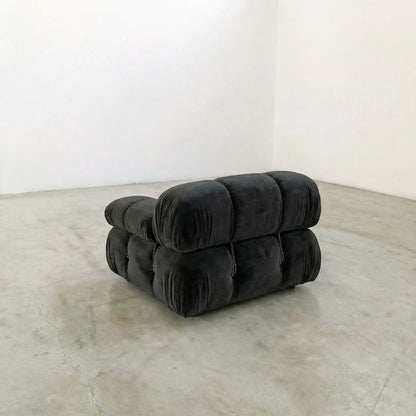 Camaleonda dupe section with armrest in dark grey velvet  in a minimalistic room with white walls and concrete floor.