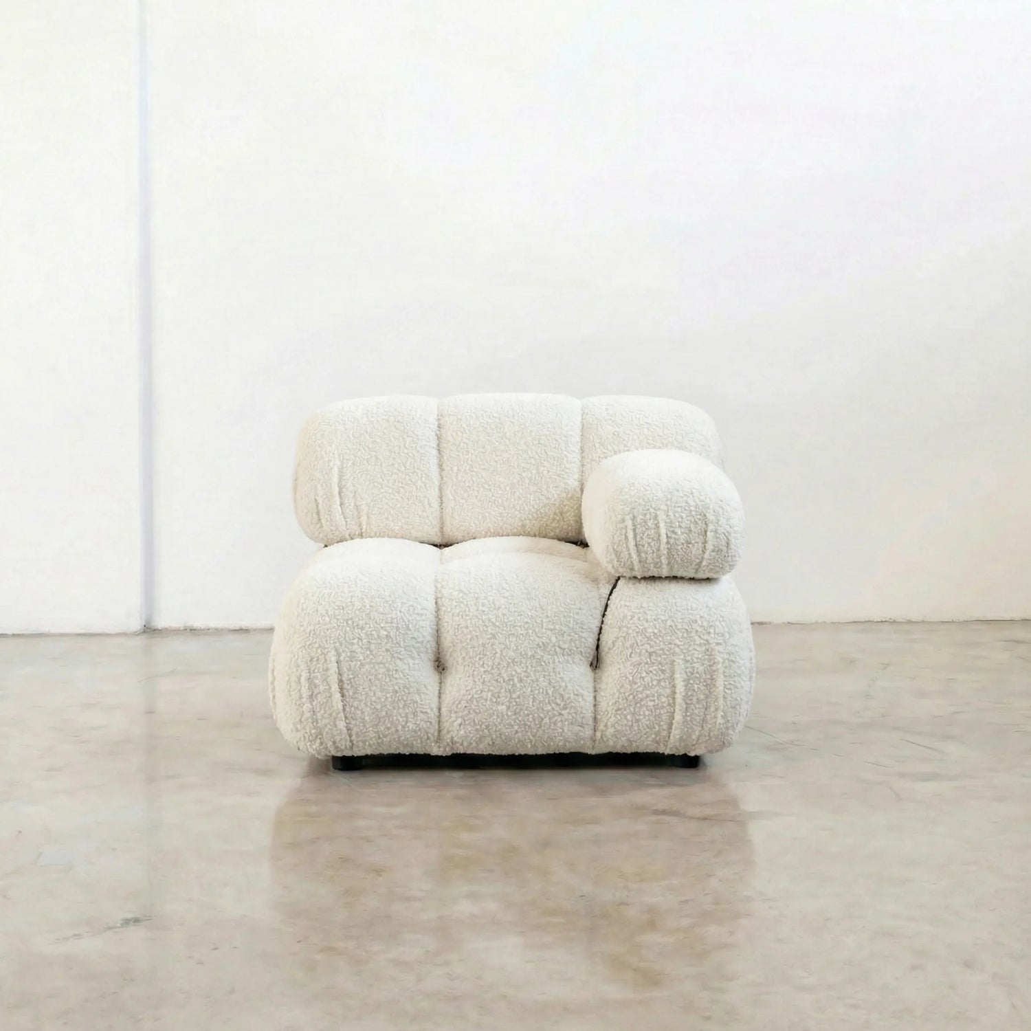 camaleonda armchair dupe with left artmrest in white bouclé in a minimalistic room with a white wall and wooden floor.