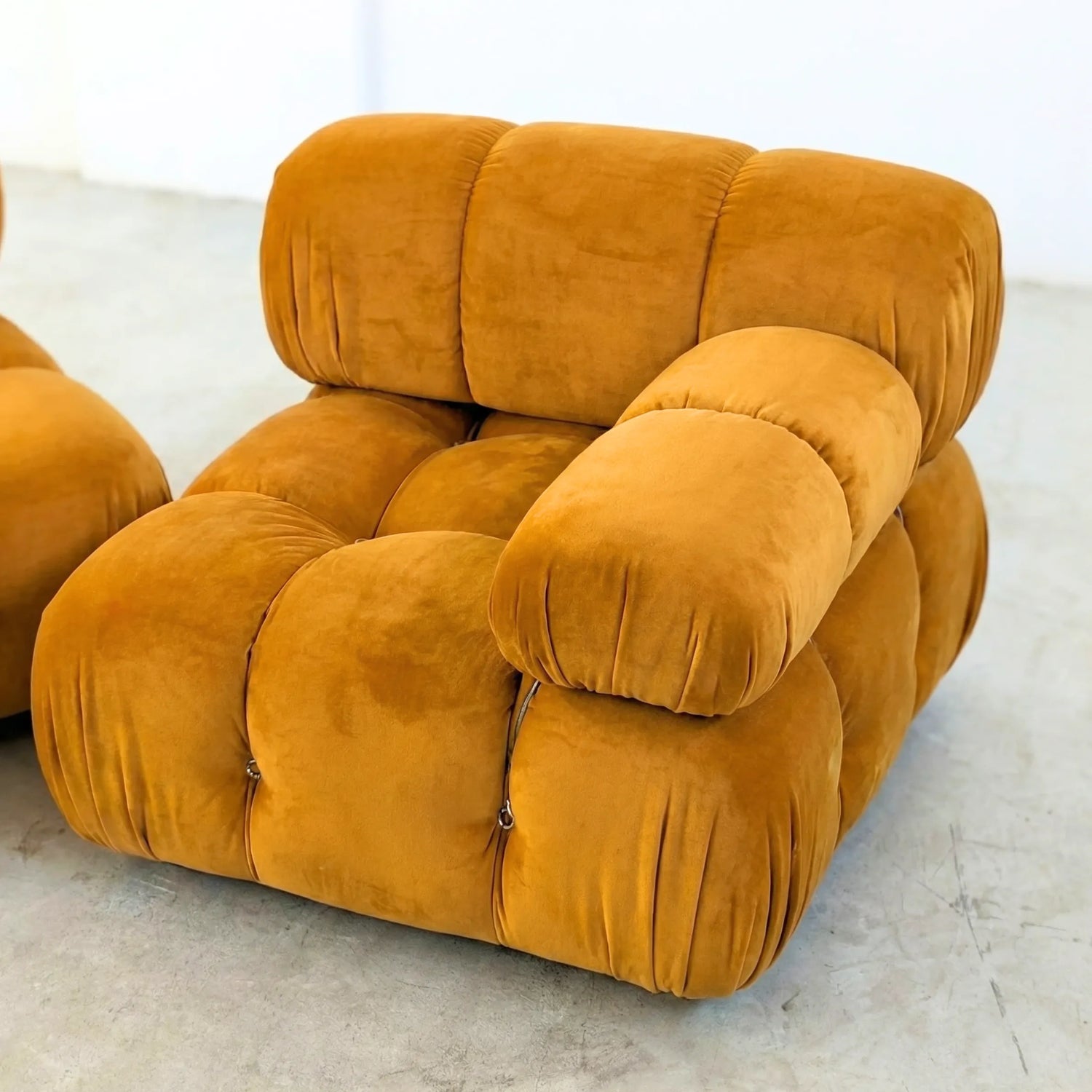 Camaleonda dupe section with armrest in mustard yellow velvet on a light gray floor with a white wall background