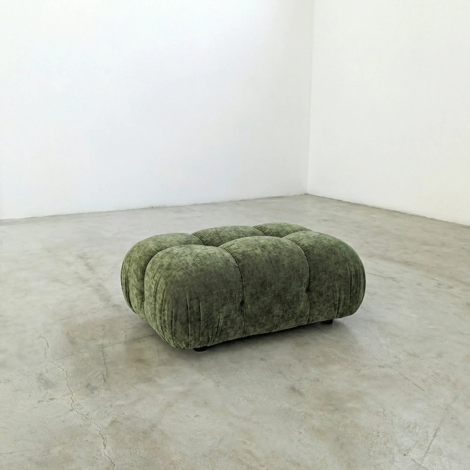 green chenille camaleonda ottoman dupe alternative on a concrete floor with white walls