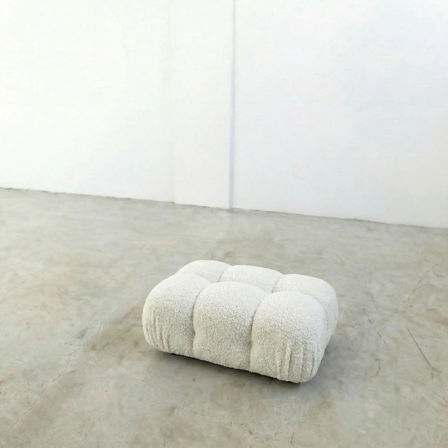 white boucle camaleonda ottoman alternative on a concrete floor with white walls