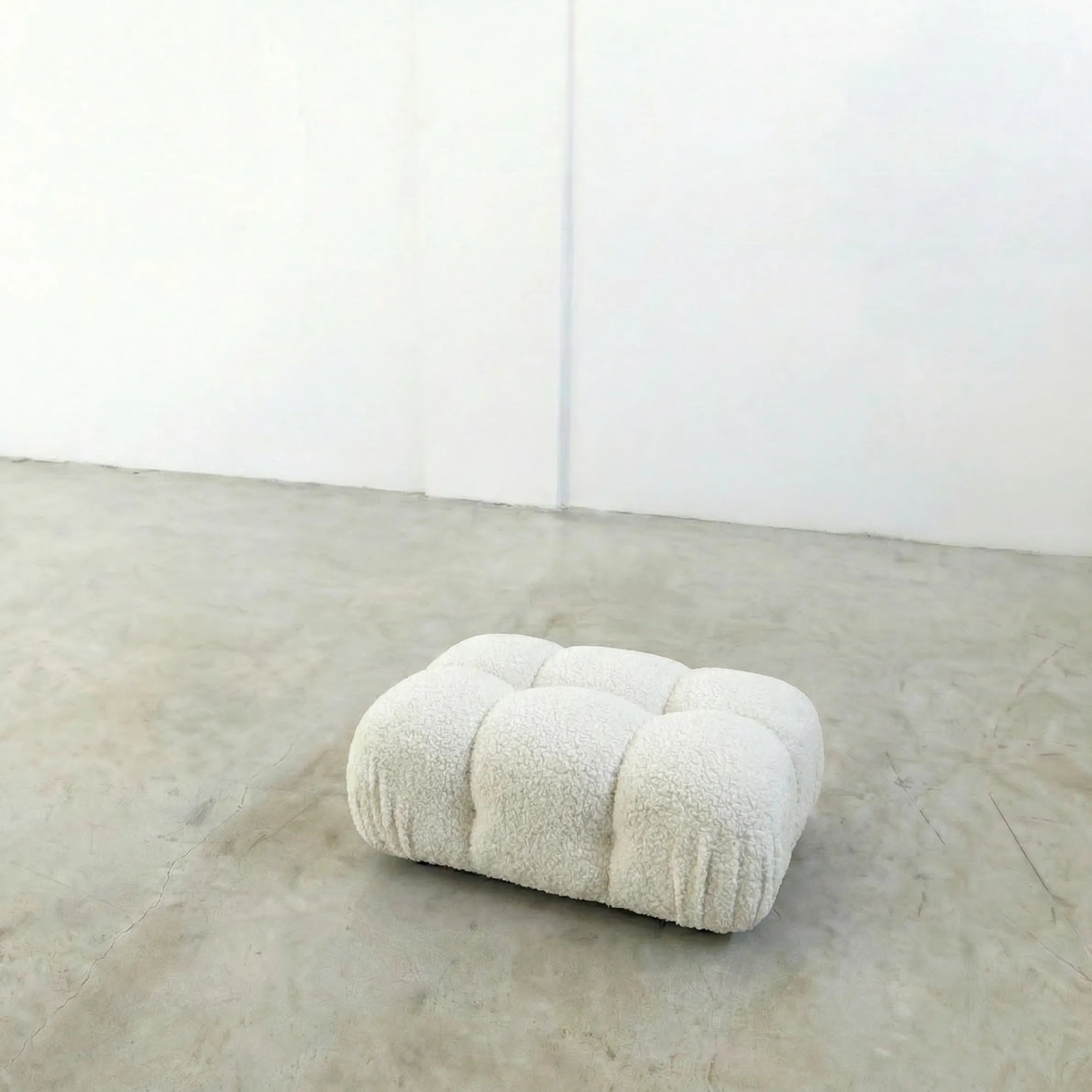 white boucle camaleonda ottoman alternative on a concrete floor with white walls