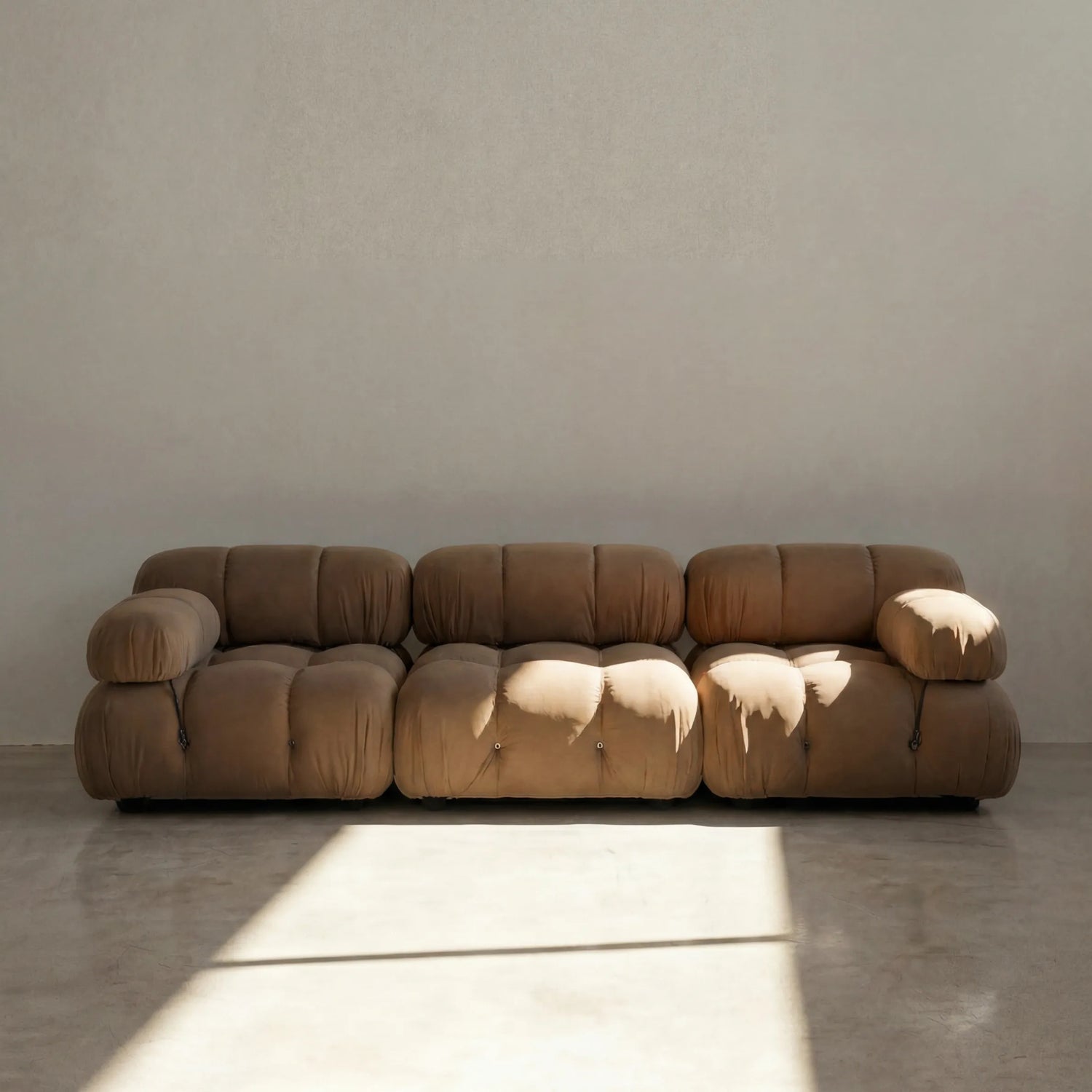 Camaleonda 3 seater modular sofa dupe in brown velvet with tufted upholstery in a minimalistic room with concrete floor and white walls