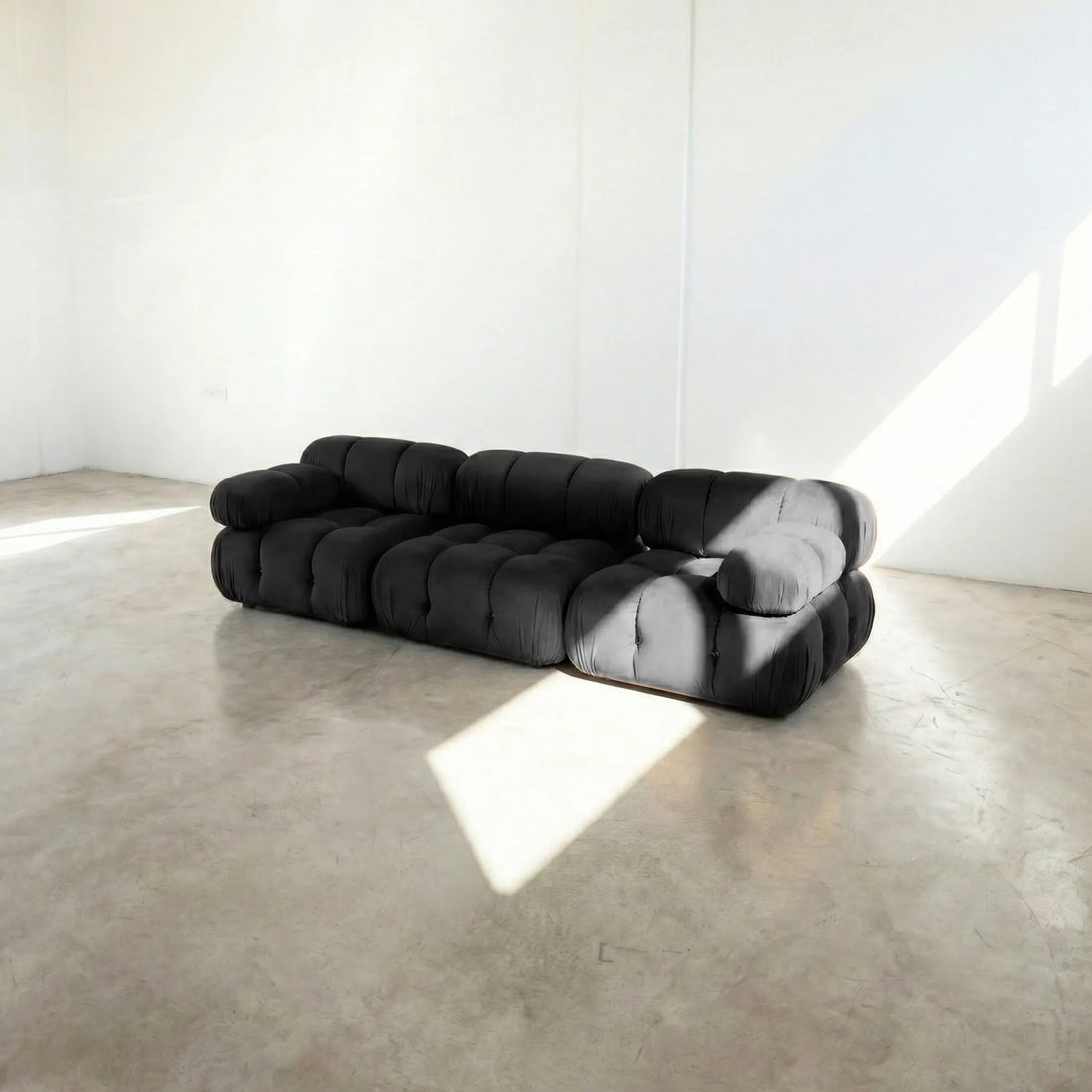 Camaleonda 3 seater modular sofa dupe in dark grey velvet with tufted upholstery in a minimalistic room with concrete floor and white walls