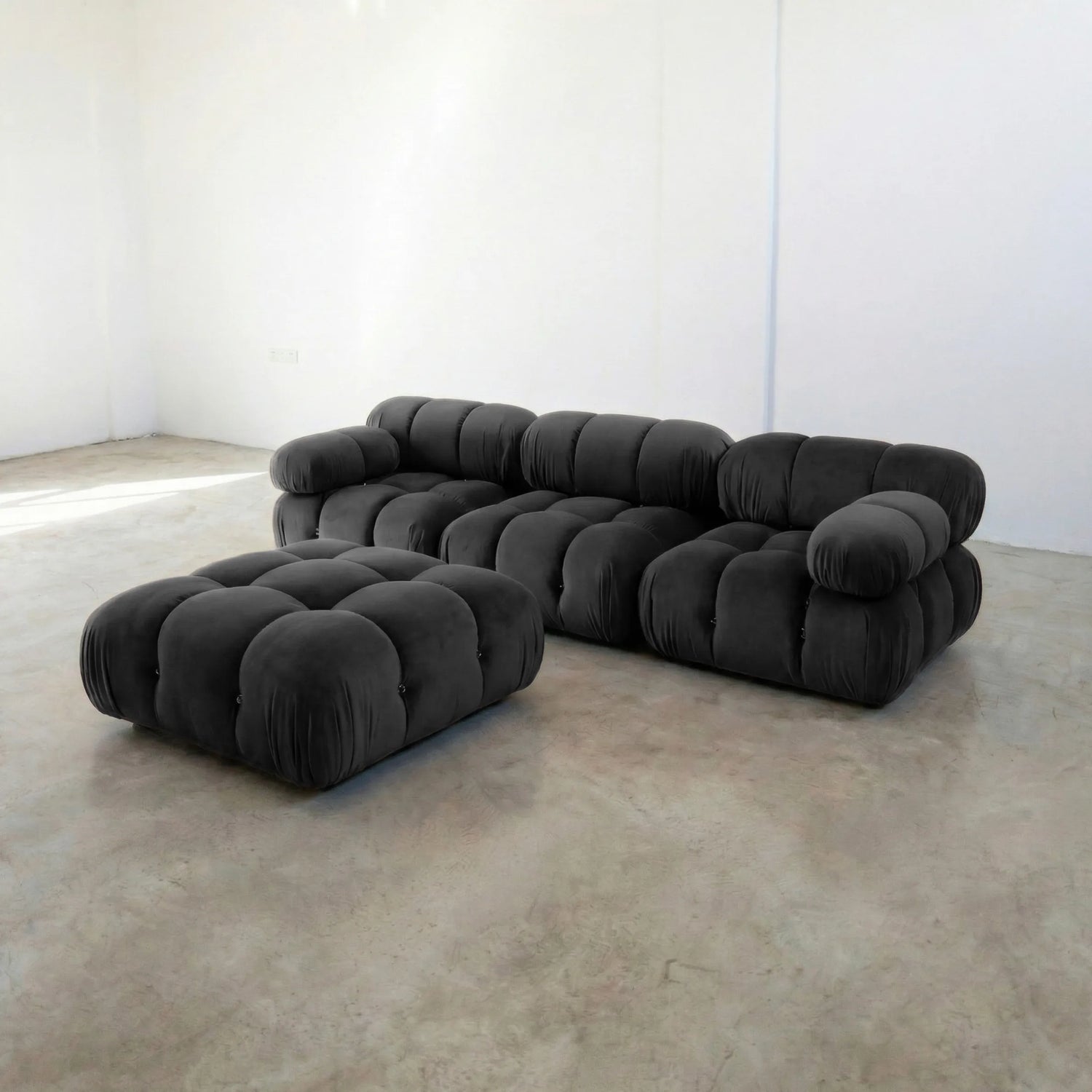Camaleonda 3 seater modular sofa dupe and ottoman in dark grey velvet with tufted upholstery in a minimalistic room with concrete floor and white walls