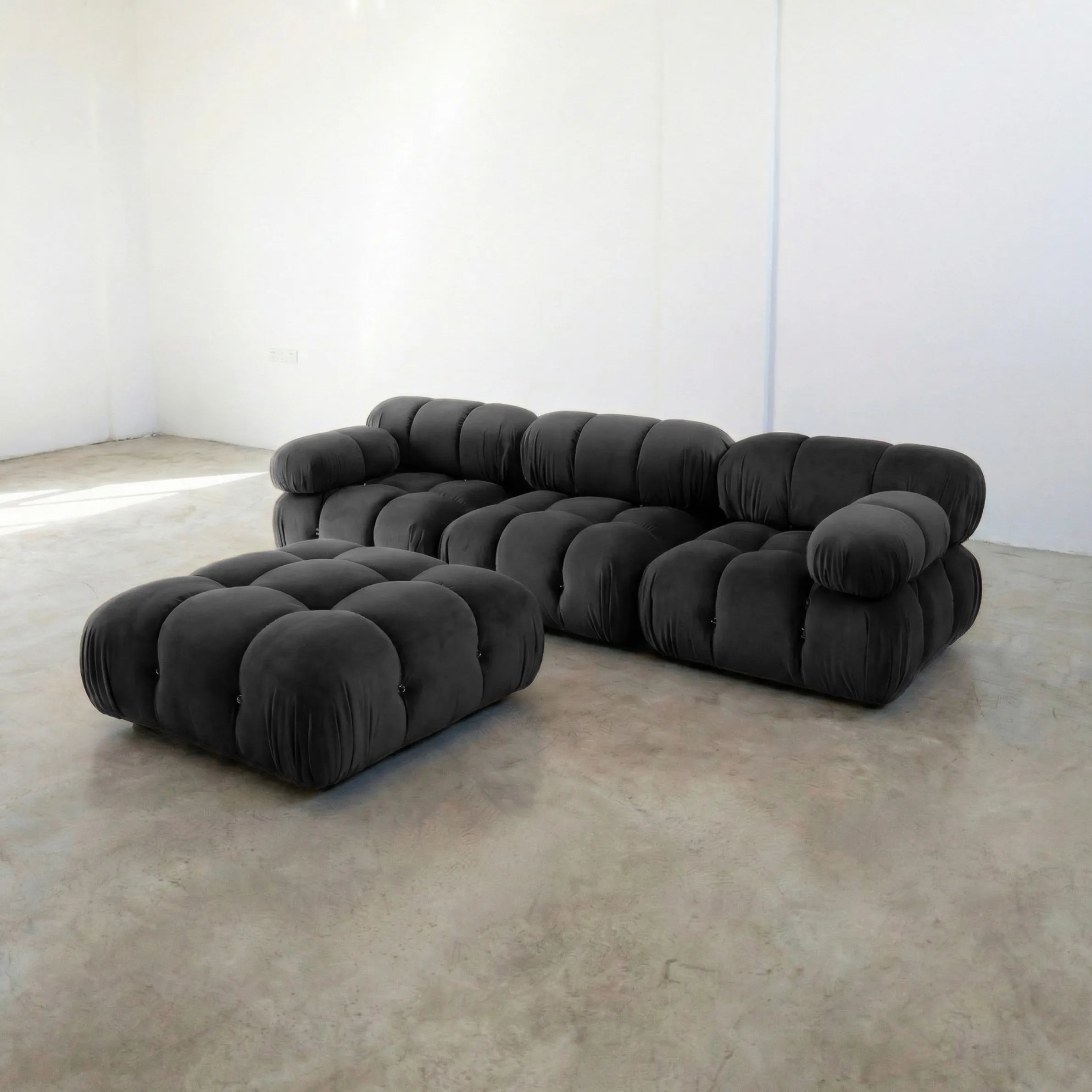 Camaleonda 3 seater modular sofa dupe and ottoman in dark grey velvet with tufted upholstery in a minimalistic room with concrete floor and white walls