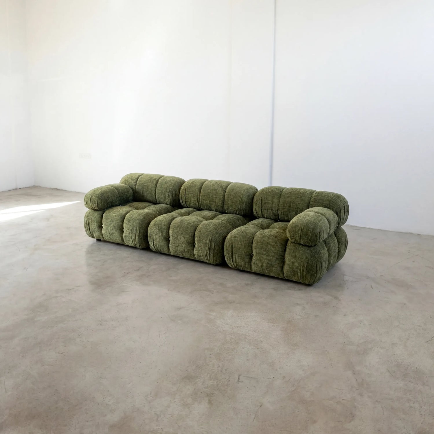 Camaleonda 3 seater modular sofa dupe in green chenille with tufted upholstery in a minimalistic room with concrete floor and white walls