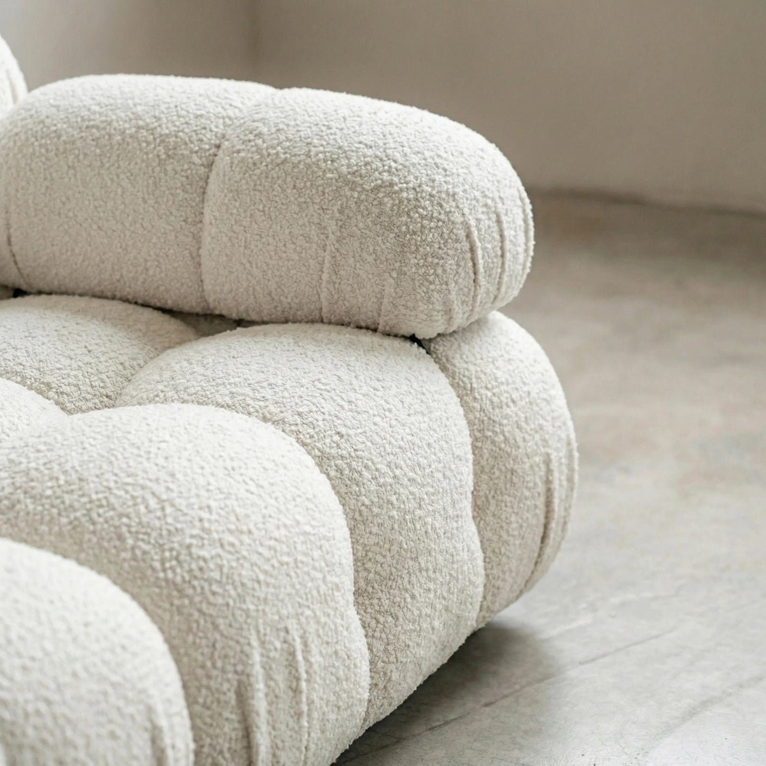 close up of Camaleonda modular sofa dupe in white bouclé with tufted upholstery in a minimalistic room with concrete floor and white walls