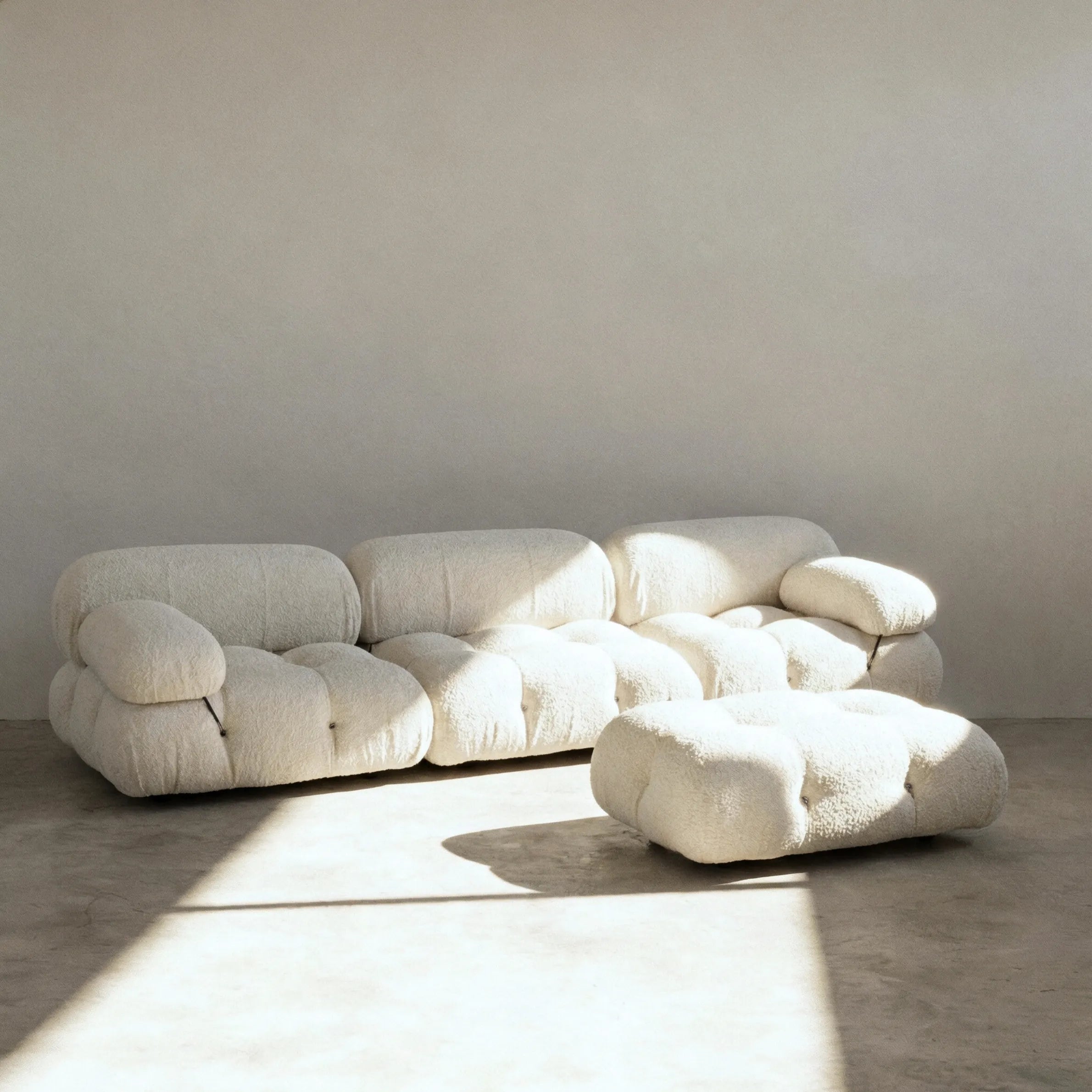 Camaleonda 3 seater modular sofa with ottoman dupe in white bouclé with tufted upholstery in a minimalistic room with concrete floor and white walls