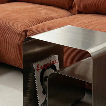 Curved metal side table with a magazine titled &