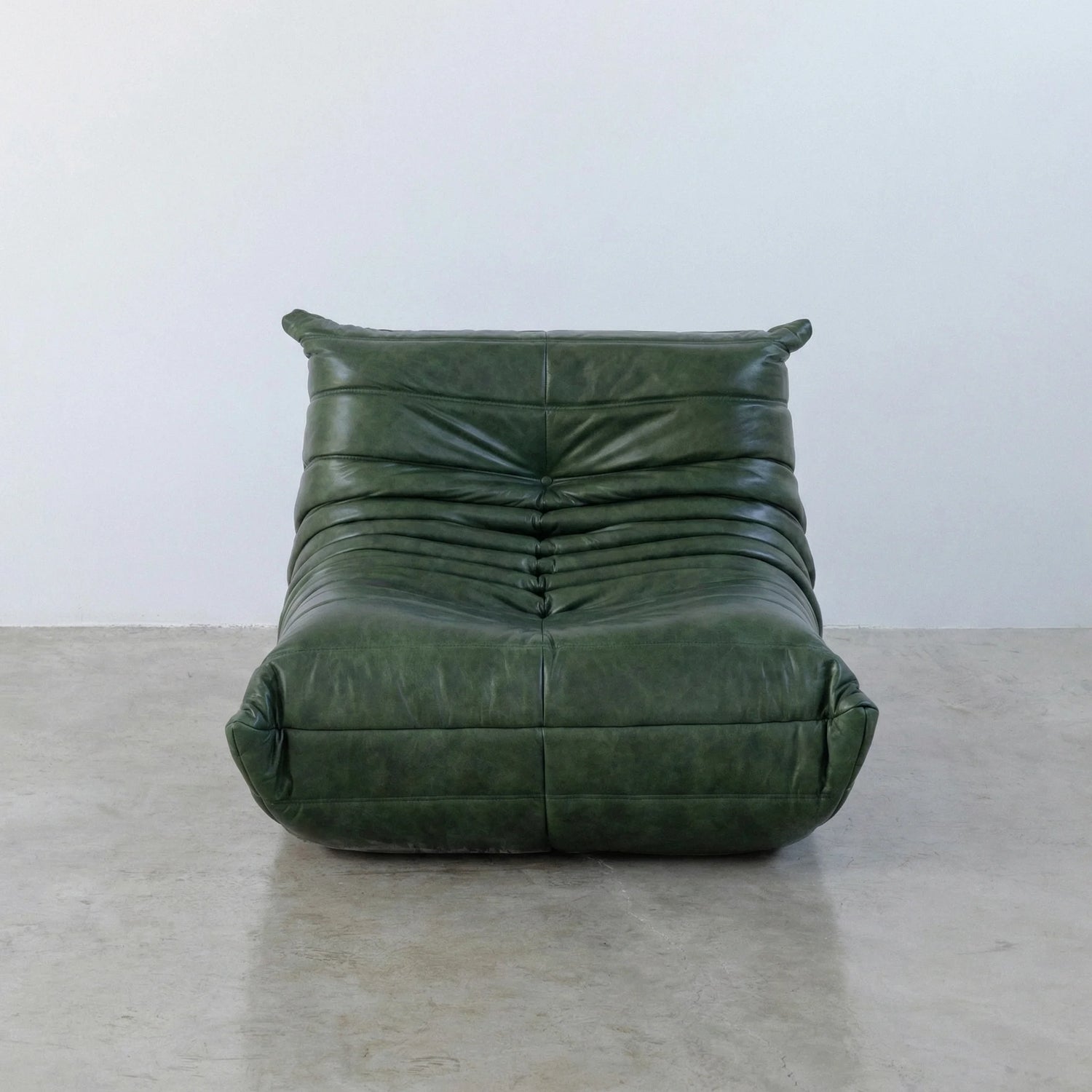 Togo Chair Dupe in green real shiny oil wax leather on a concrete floor with a white wall background