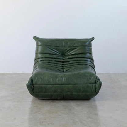 Togo Chair Dupe in green real shiny oil wax leather on a concrete floor with a white wall background