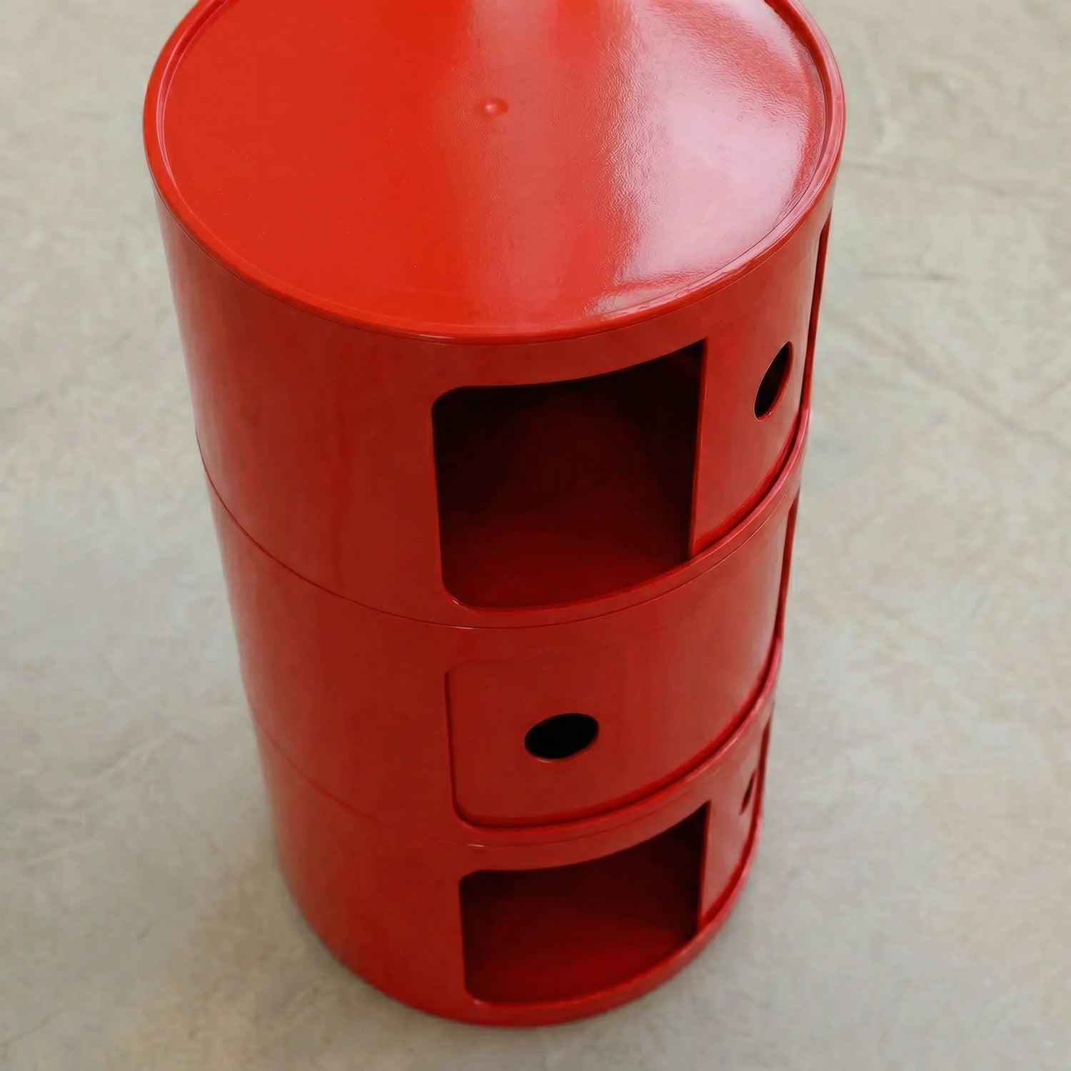 Red glossy round modular storage unit, Kartell Componibili dupe with three tiers in minimalist concrete studio, 35mm shot
