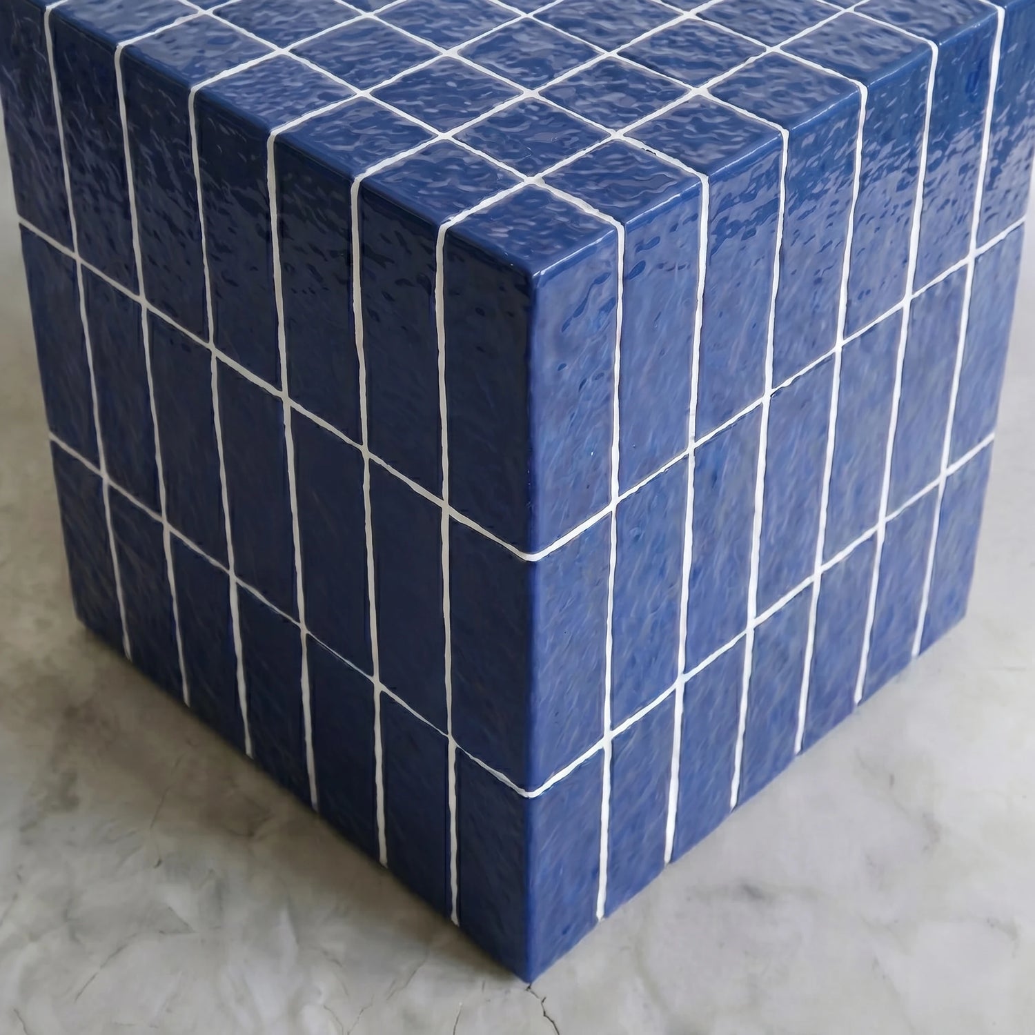 Close-up of the glazed blue cube side table corner showing the hand-finished ceramic-look surface.