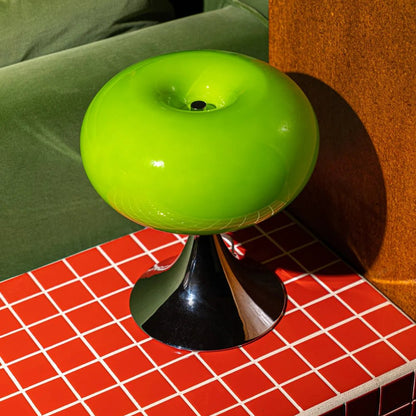 Retro space age table lamp in green placed on electric red tiles, inspired by 70s globe lighting.