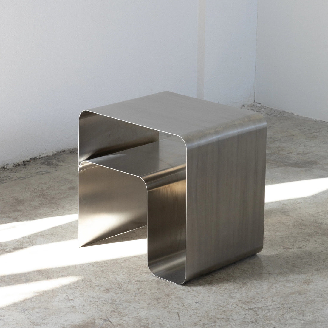 metal stainless steel side table on a concrete floor with a white wall background