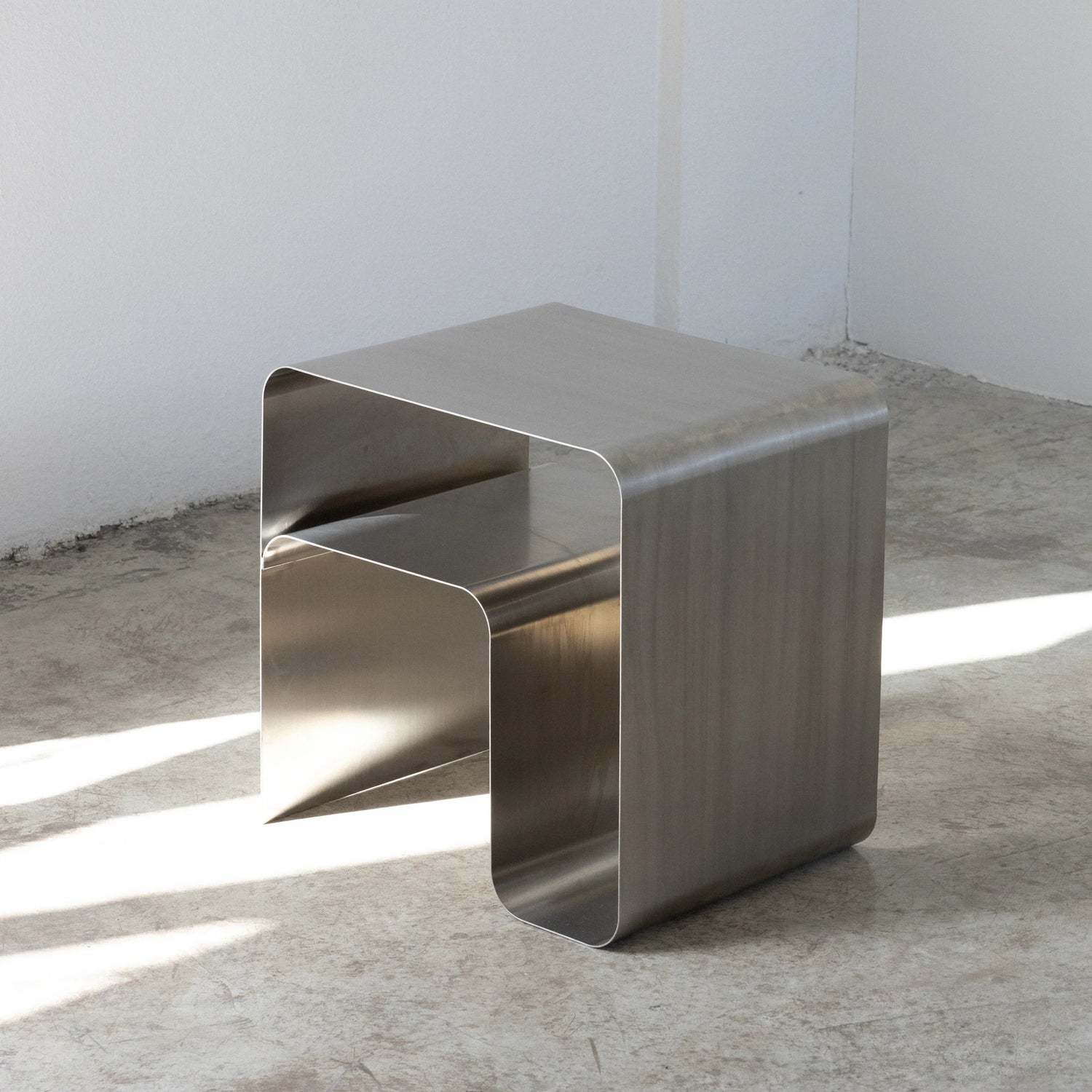 metal stainless steel side table on a concrete floor with a white wall background