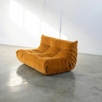 Mustard yellow dupe of the Togo Sofa silhouette designed by michael ducaroy for ligne roset – custom-made yellow velvet seating for modern interiors on a concrete floor with white walls