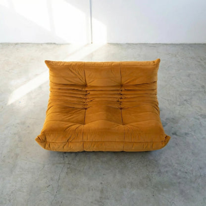 Mustard yellow dupe of the Togo 2-seater Sofa silhouette designed by michael ducaroy for ligne roset – custom-made yellow velvet seating for modern interiors on a concrete floor with white walls