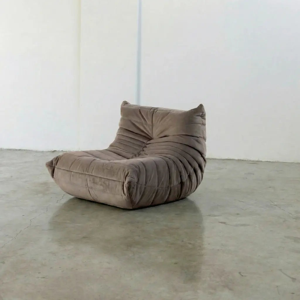 Togo Chair Dupe in taupe, brownish color made from velvet suede by vibehaus, on a concrete floor with a white wall background