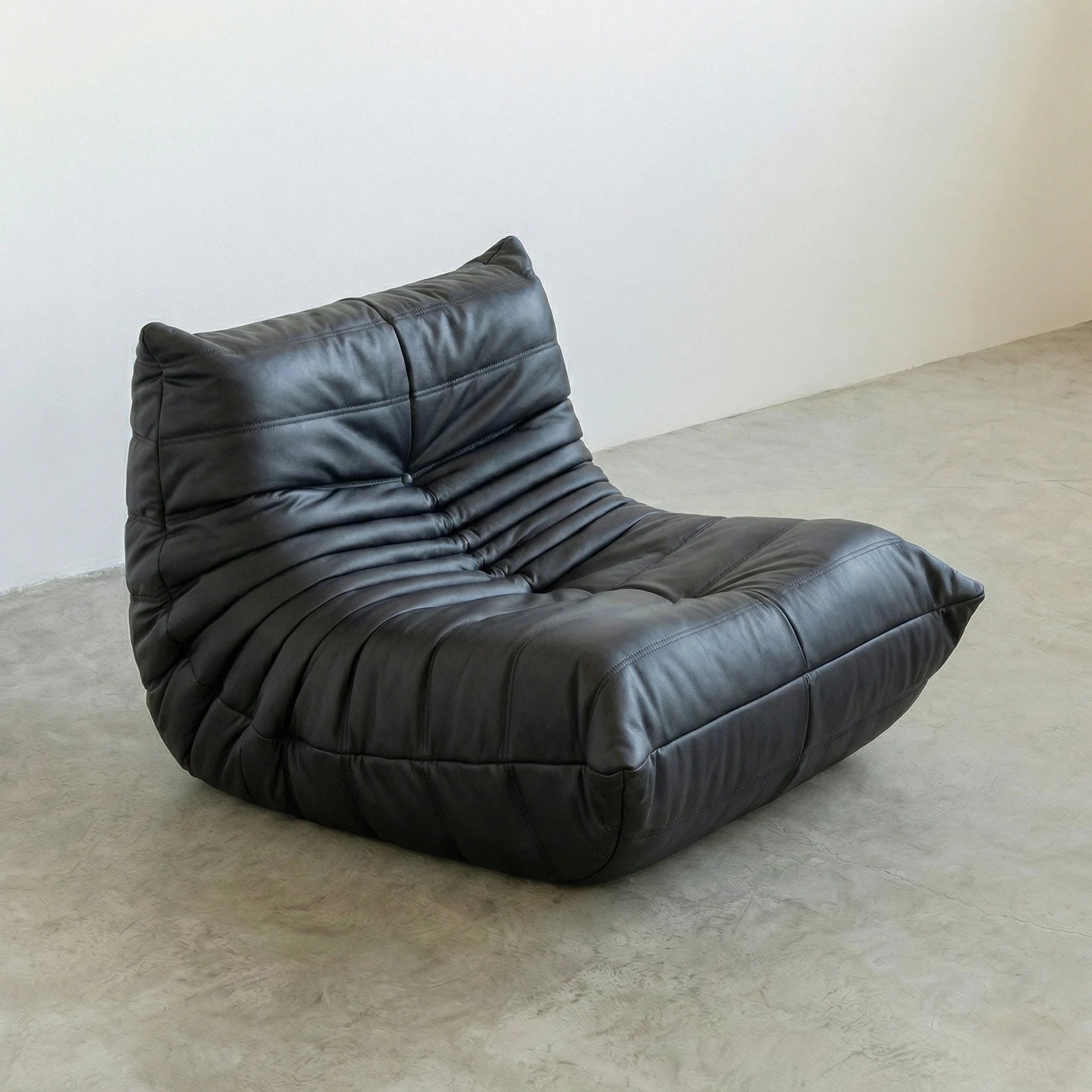 Togo Chair Dupe in black faux leather on a concrete floor with a white wall background