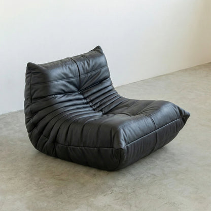 Togo Chair Dupe in black faux leather on a concrete floor with a white wall background