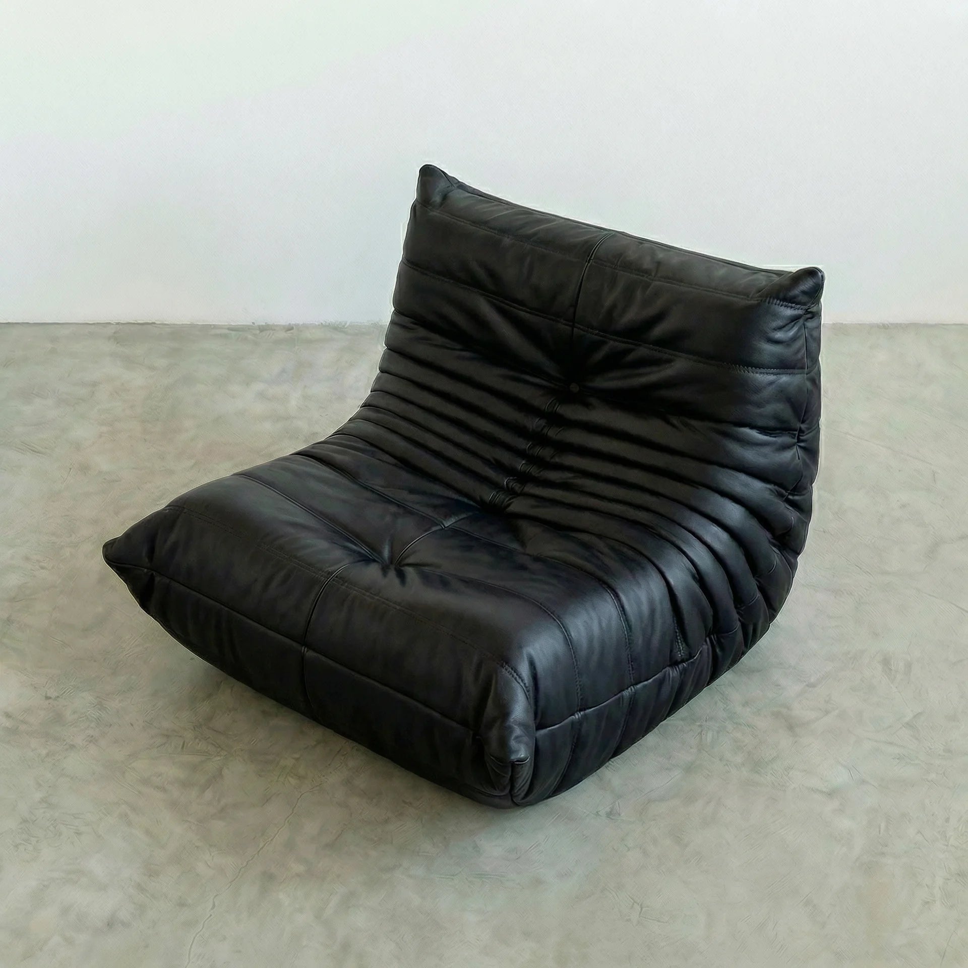 Togo Chair Dupe in Black faux leather on a beige floor with a white wall background