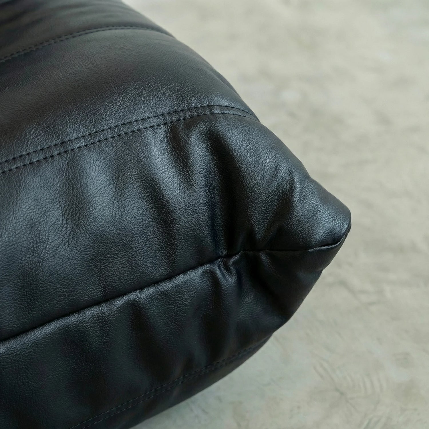 Close-up of a black leather togo couch dupe on a concrete floor.
