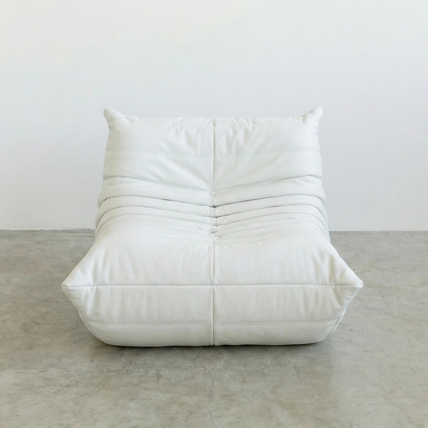 Togo Chair Dupe in white faux leather on a concrete floor with a white wall background