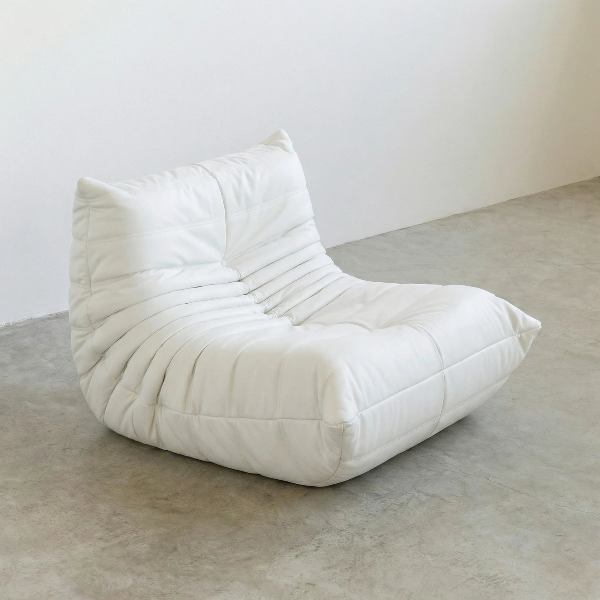 Togo Chair Dupe in white faux leather on a concrete floor with a white wall background