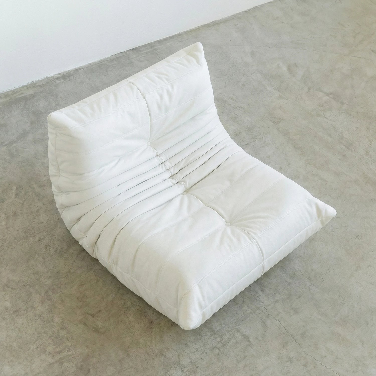 Togo Chair Dupe in white faux leather on a concrete floor with a white wall background by vibehaus