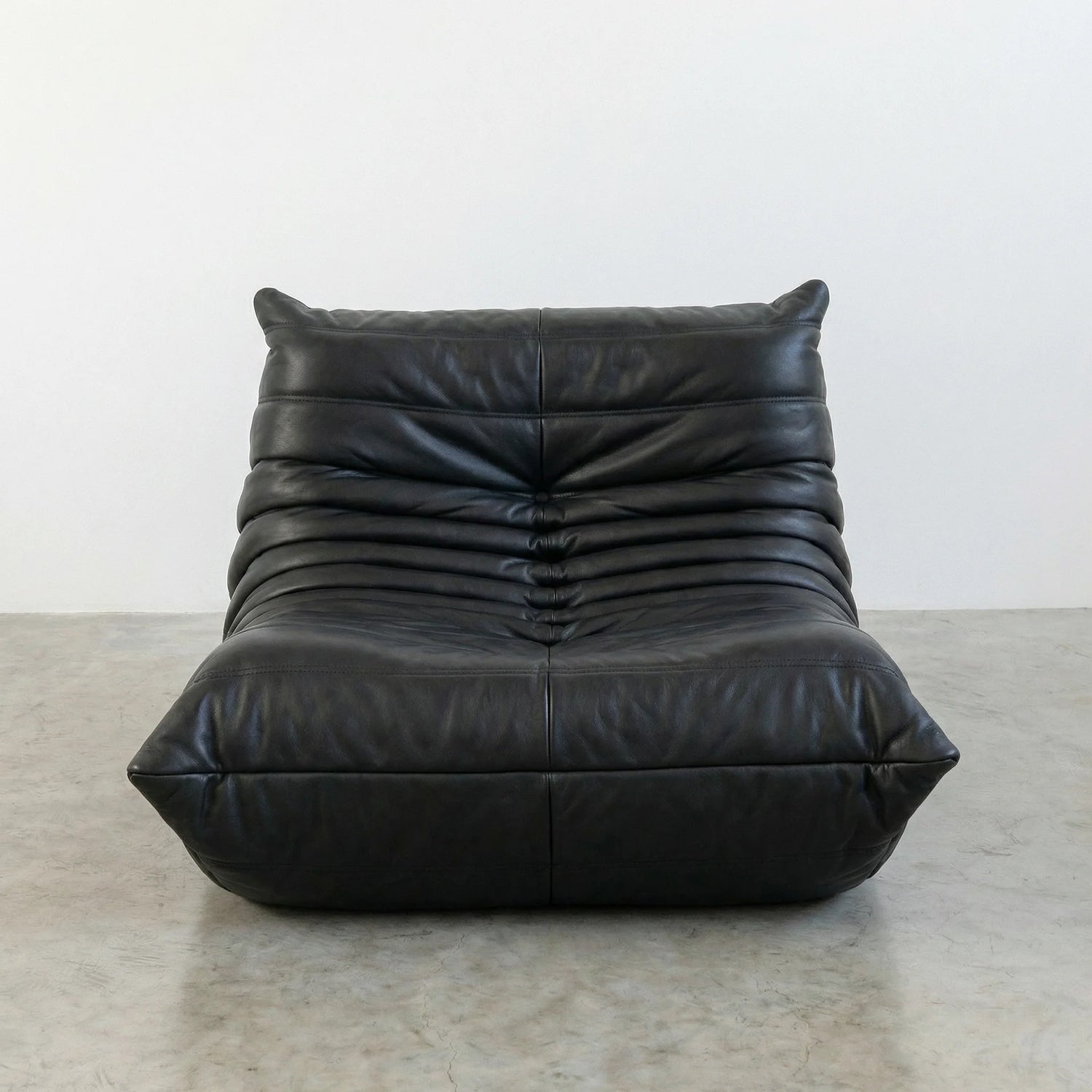 Togo Chair Dupe in black real cowhide leather on a concrete floor with a white wall background
