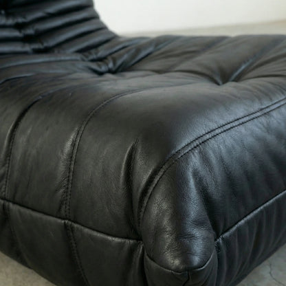 Close-ip of the Togo Chair Dupe in black real cowhide leather on a concrete floor with a white wall background