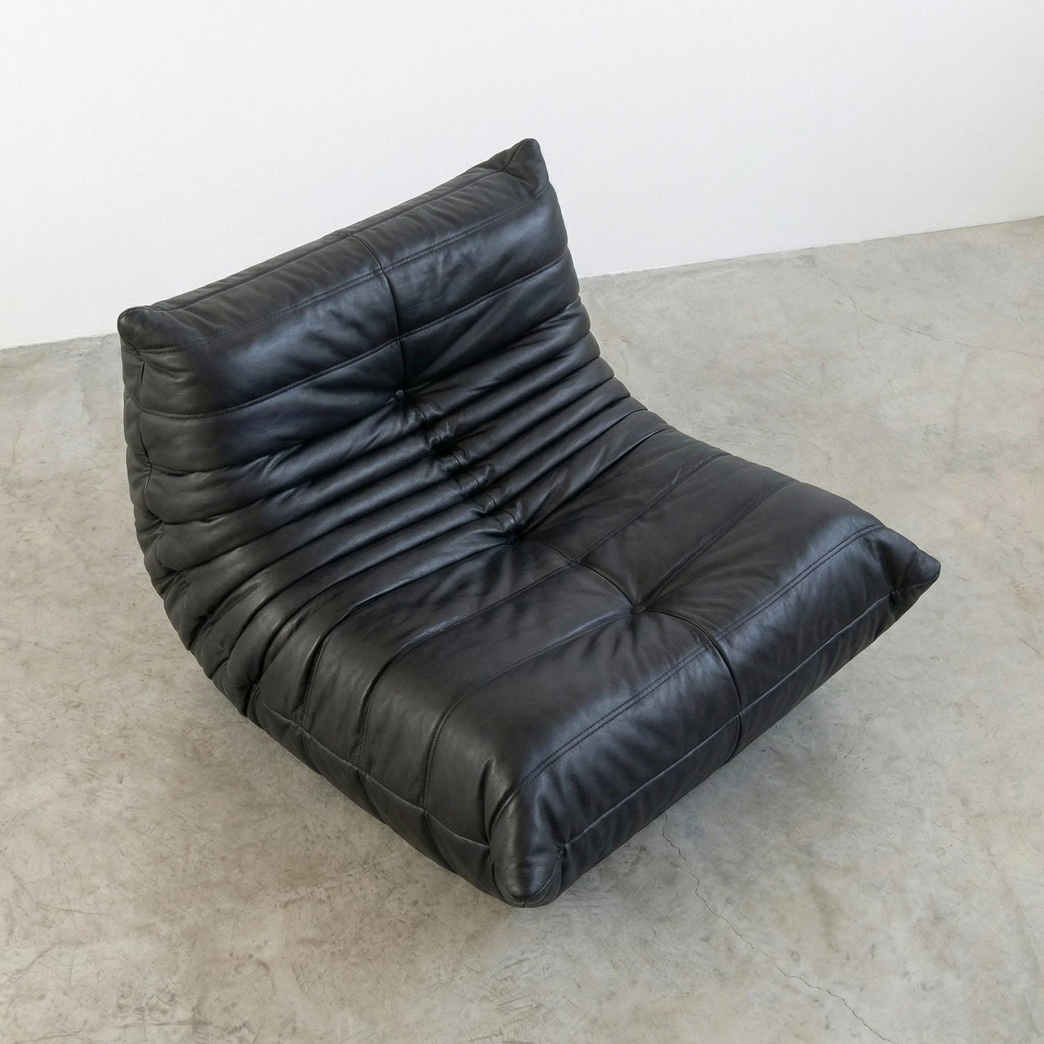 Togo Chair Dupe in black real cowhide leather on a concrete floor with a white wall background
