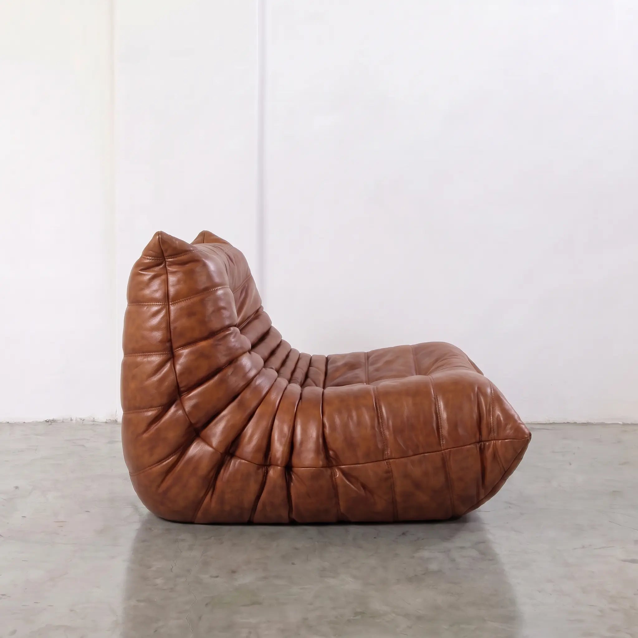 Togo dupe chair in brown real waxed leather on a light gray floor with a white wall background