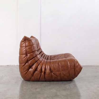 Togo dupe chair in brown real waxed leather on a light gray floor with a white wall background