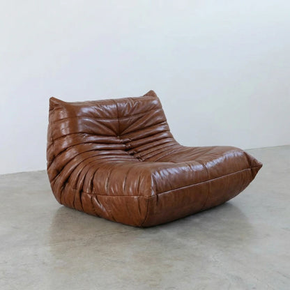 Togo Chair Dupe in brown real shiny oil wax leather on a concrete floor with a white wall background